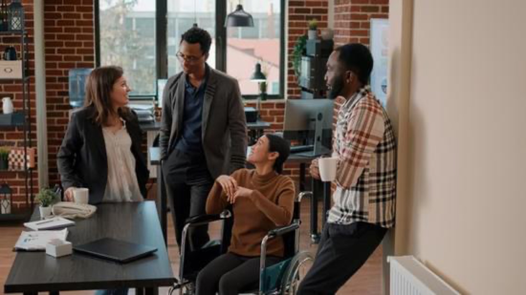 Quatre collègues, dont une collaboratrice en fauteuil roulant, échangent autour d’une table de réunion